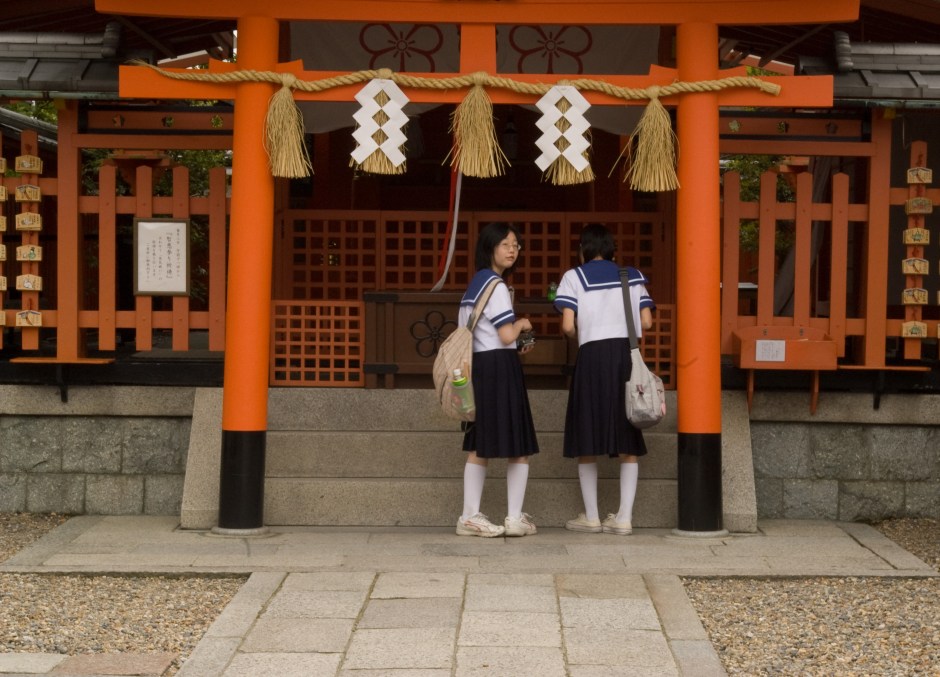 Young girls offer prayers and bows at a Torii Gate in a Shinto shrine