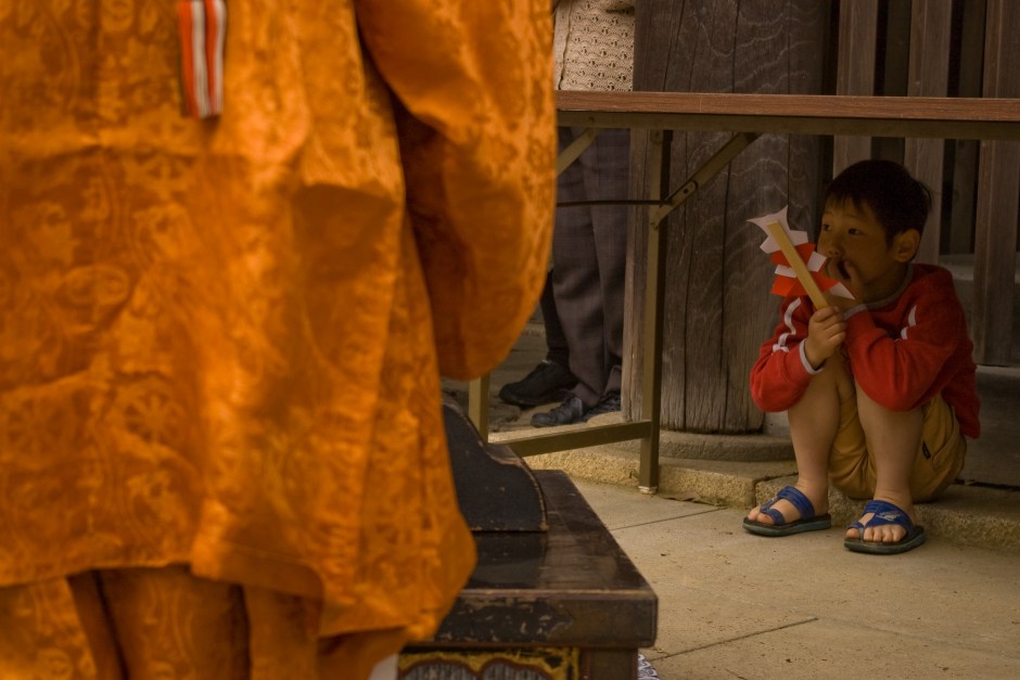 A young boy clutches a prayer stick and looks on to a Shinto spring ceremony