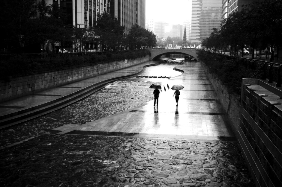 People stroll along the Cheonggyecheon, despite the rain