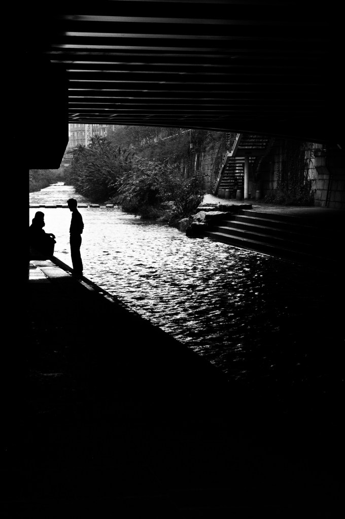An elderly couple relaxes under a bridge on a rainy holiday
