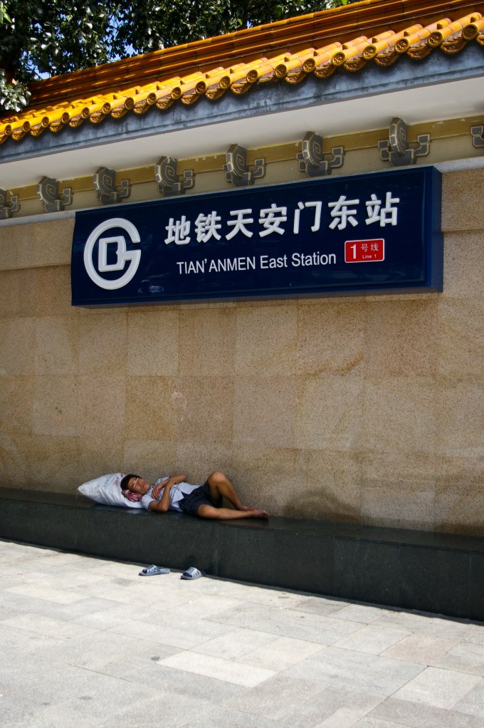 A man rests in the shade of the Tian'anmen Station
