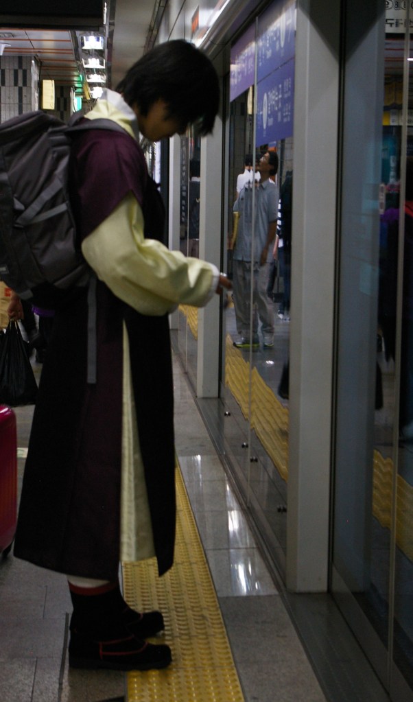 A young man in traditional Korean clothing waits for the subway