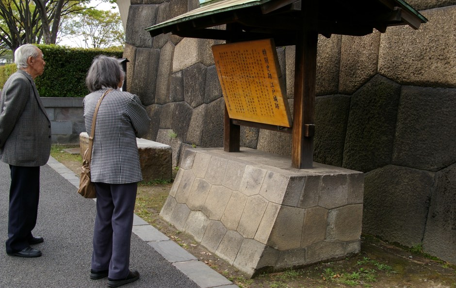 An elderly couple reads a plaque as they enter the Kokyo Gaien National Garden